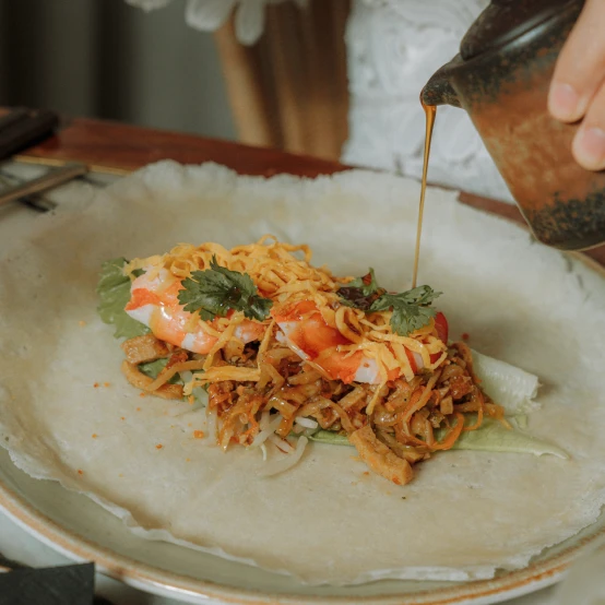 person pouring sauce onto a popiah shrimp