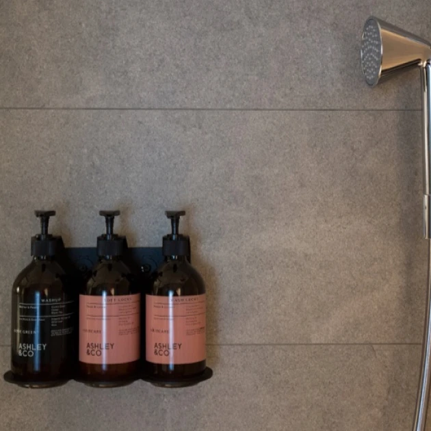 three bottles of toiletries on a shower shelf