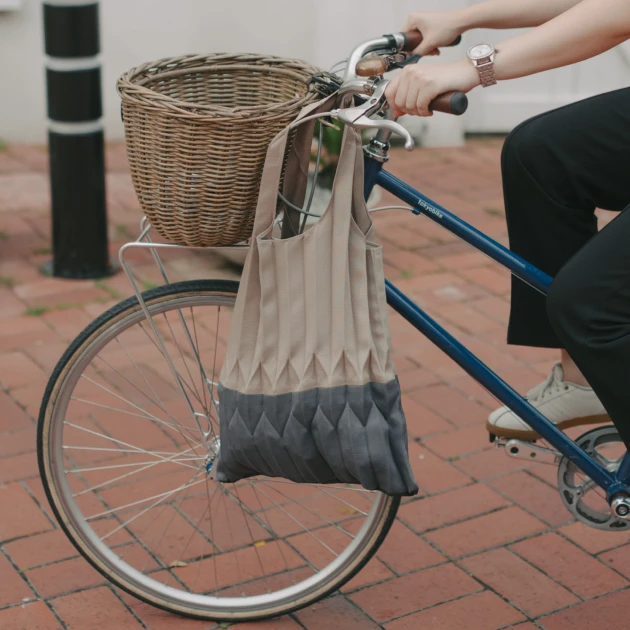 a person riding a bicycle with a basket and tote bag hanging from the side