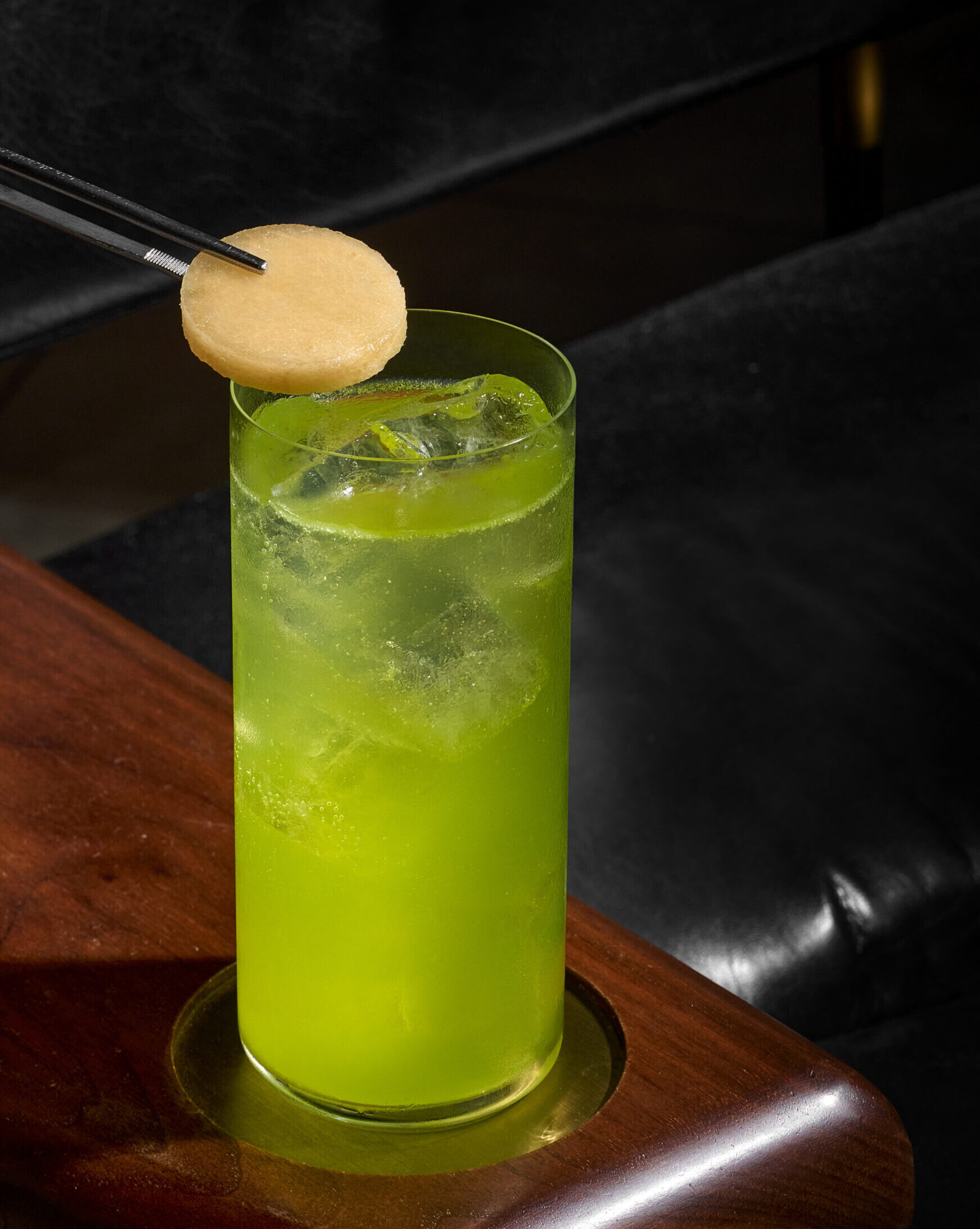 green coloured drink in a tall glass cup with a person putting a topping in
