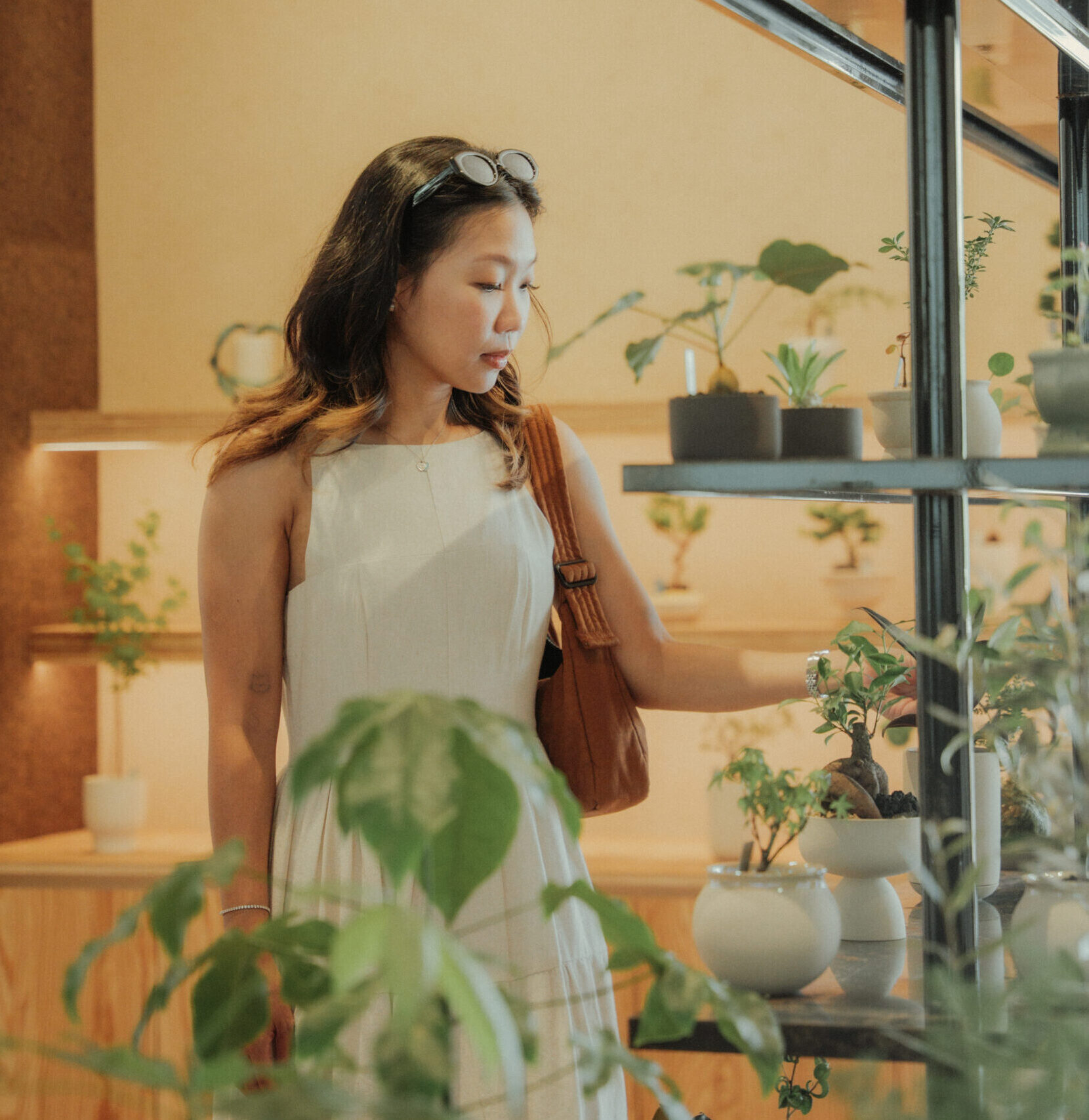 woman in a white dress looking plants on a shelf in a plant shop
