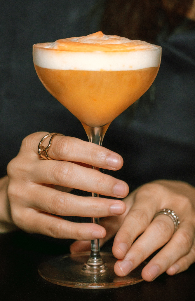 person holding an orange coloured drink in a glass cup