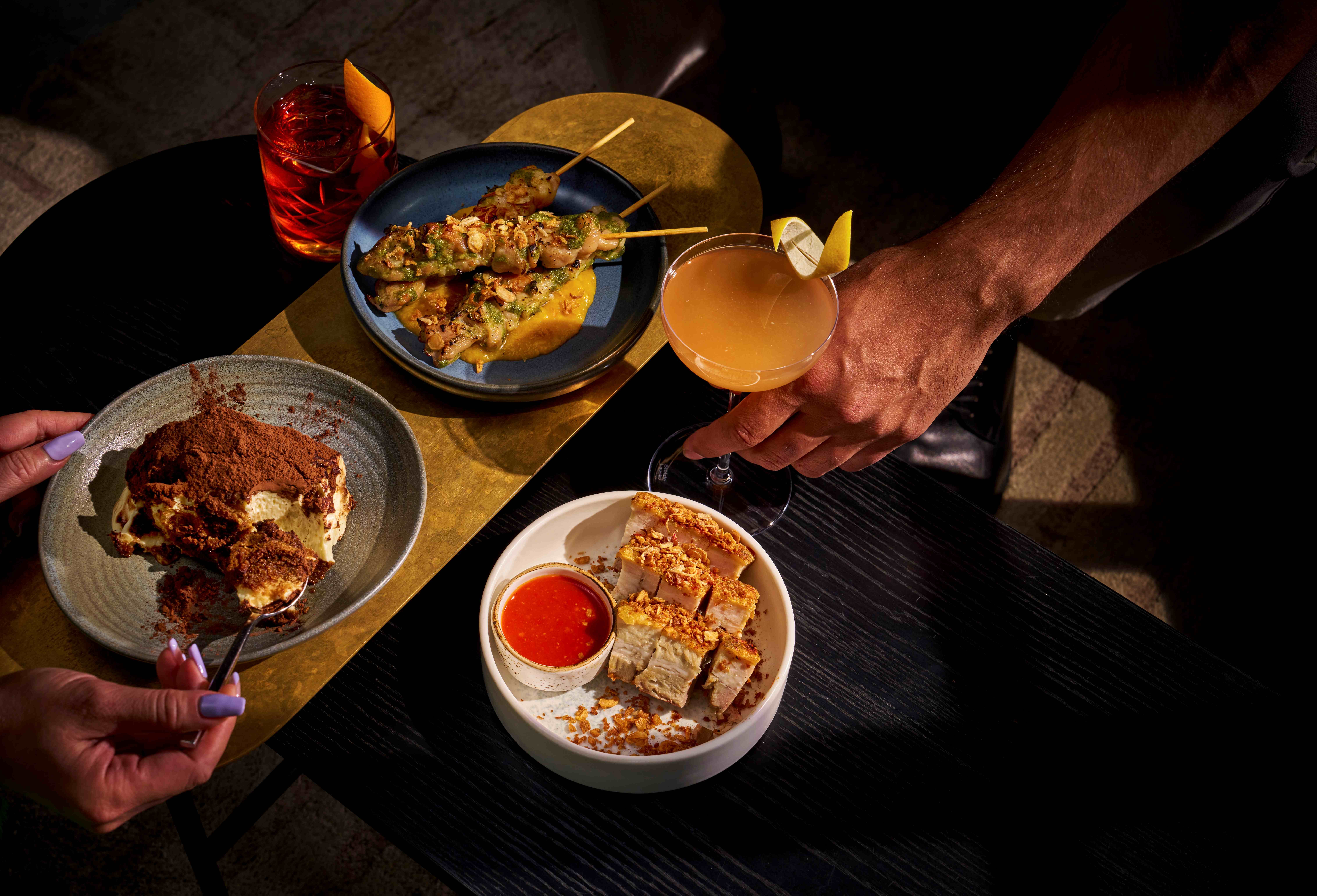 two people sharing a few dishes on a black wooden table